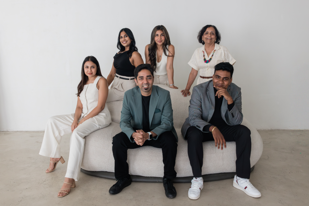 The Shaadi Baraat & Co team of six — four women and two men in neutral tailoring, gathered around a cream sofa in a bright studio